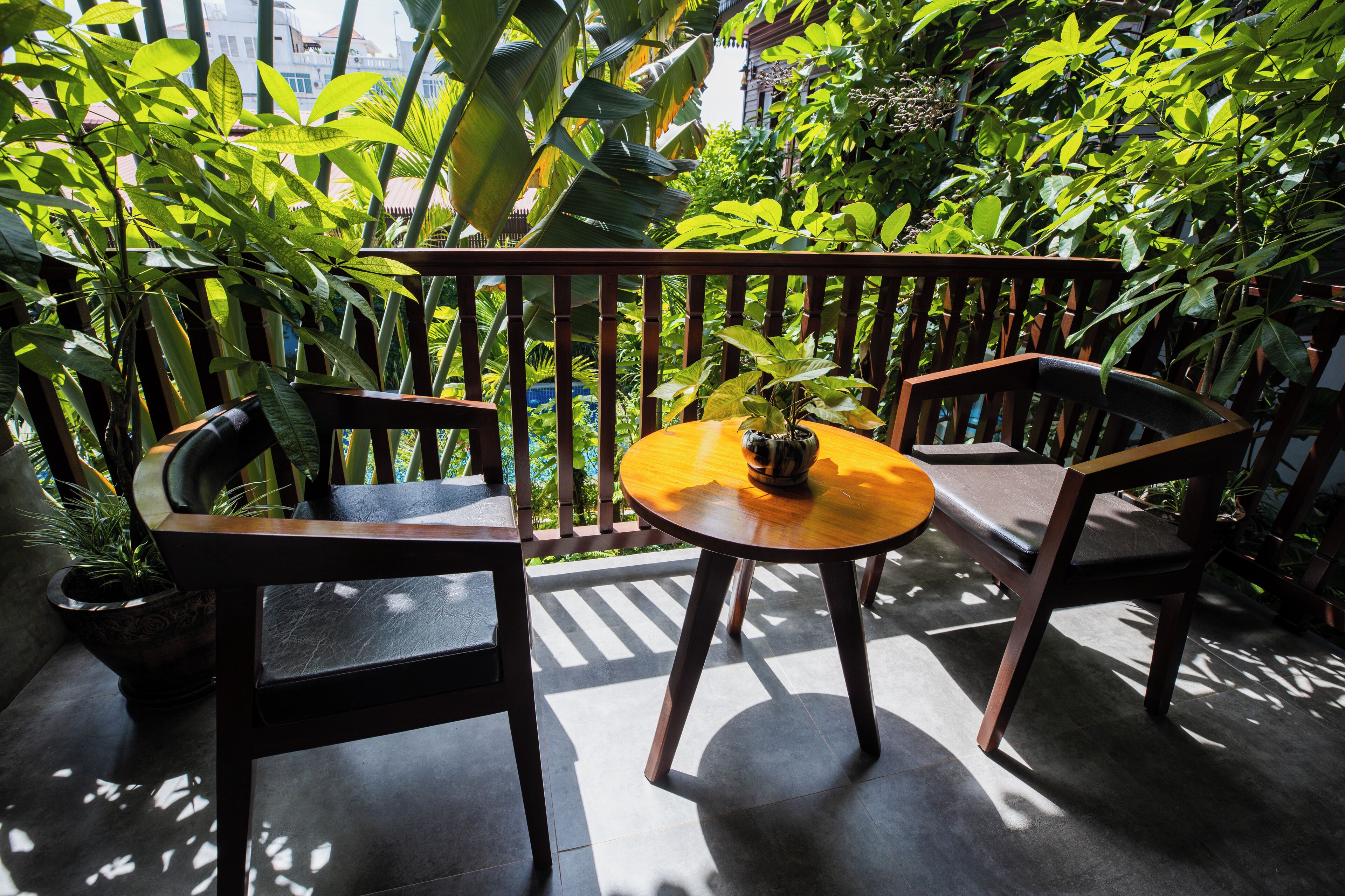 A wooden bench with a small table and a potted plant in a lush, green outdoor area.