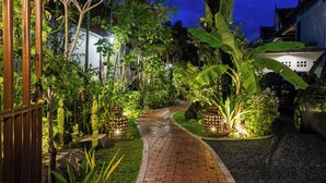 A paved pathway in a garden area with plants and a vehicle parked nearby. - Golden Vishnu Villa (Siem Reap)