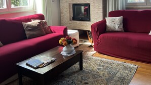 Una sala de estar con chimenea, sofás rojos, una mesa de centro con un florero y una alfombra estampada.