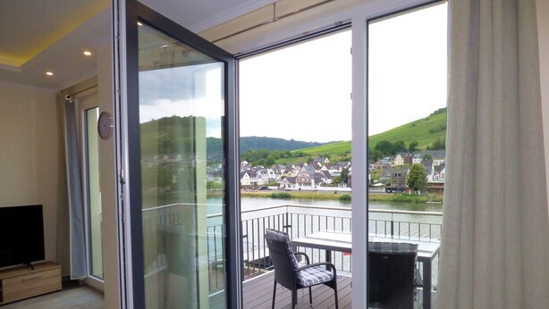 A modern room with a sliding glass door leading to a balcony with a view of a river and a town.