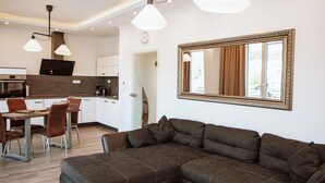 A modern living room with a sectional sofa, a dining area with chairs, and a kitchen in the background.