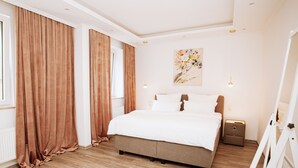 A bedroom with a large bed, a white rug, wooden flooring, and a painting on the wall.