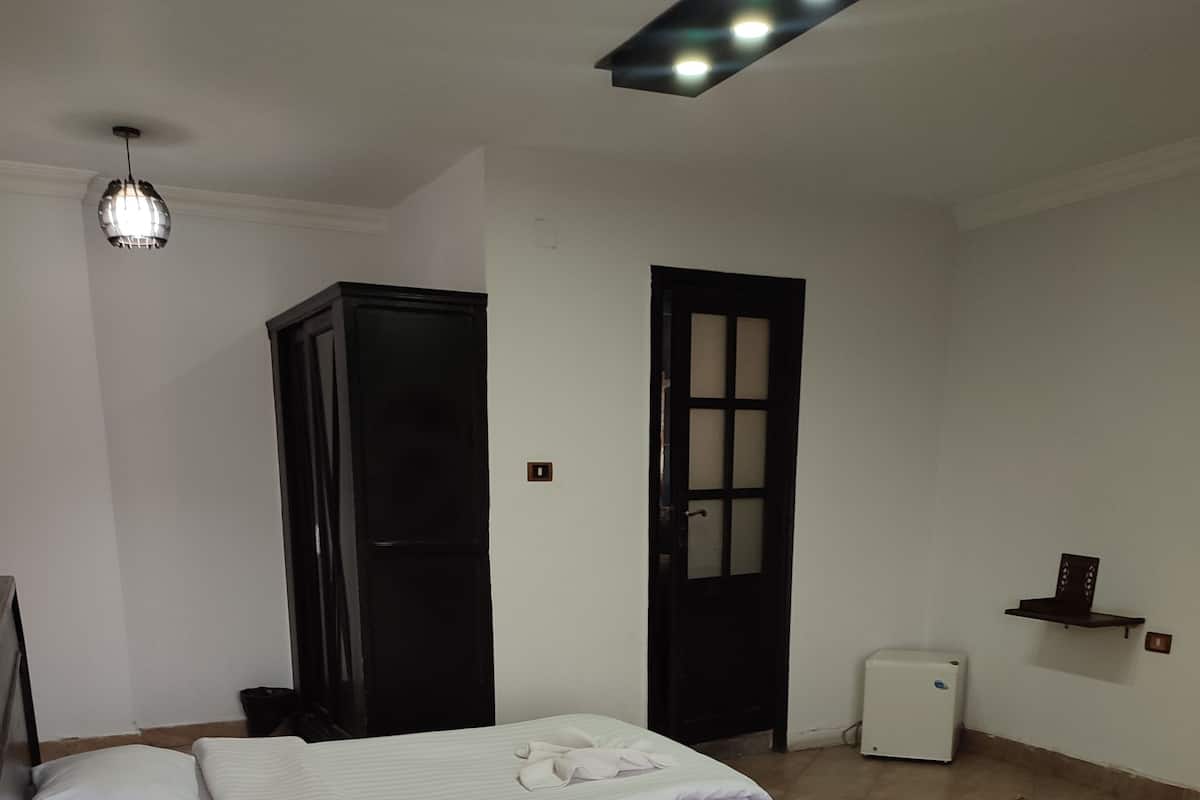 A hotel room with two beds, a wardrobe, a door, a small table with a remote control, and a refrigerator.