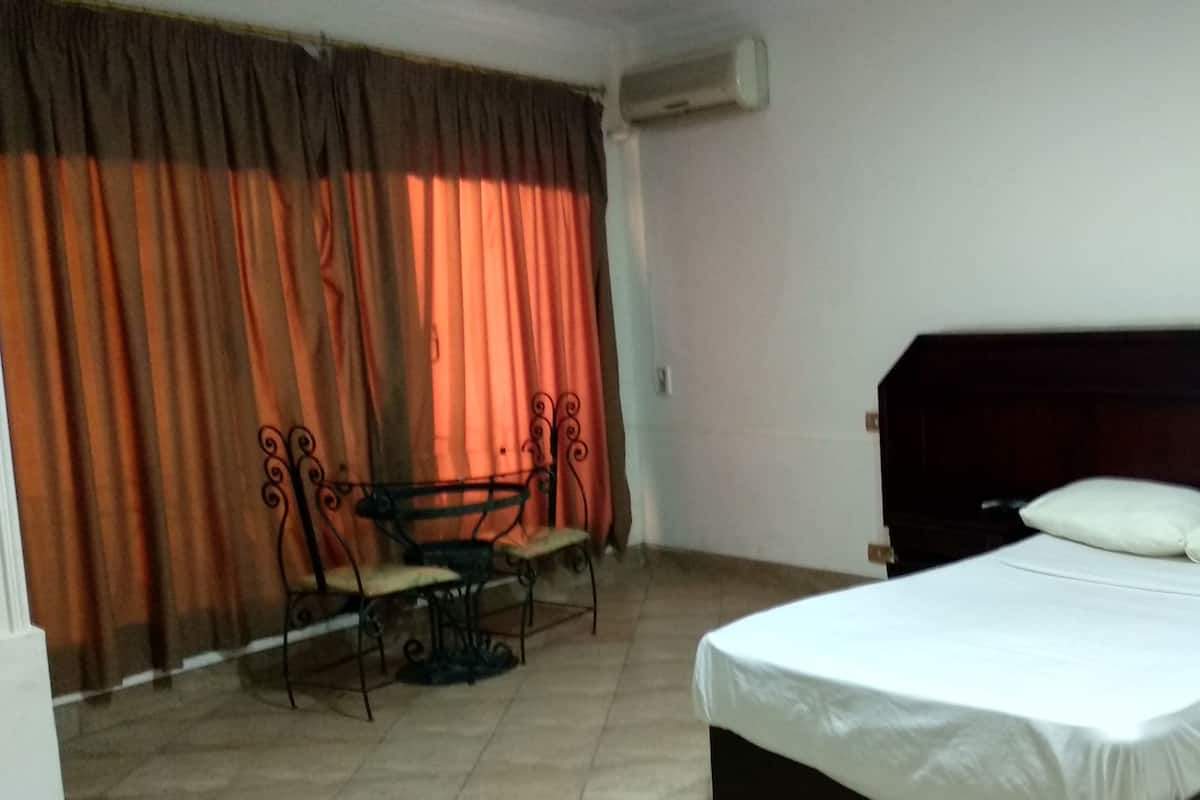 A bedroom with a bed, curtains, a table with chairs, and an air conditioning unit.