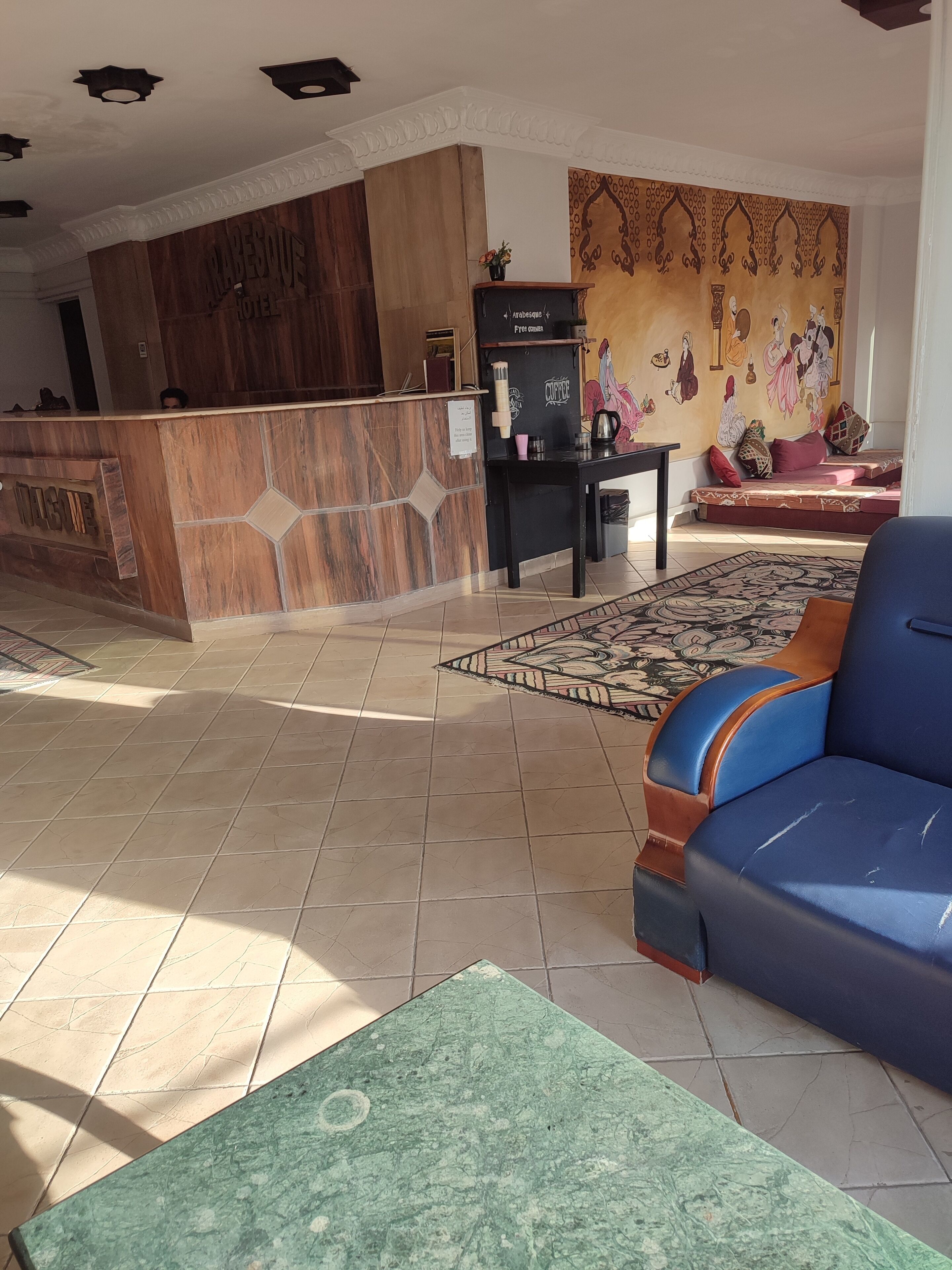 Un hall d’hôtel comprenant un comptoir d’accueil, un coin café, un tapis à motifs et un canapé bleu.