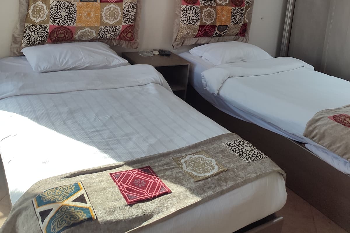 A hotel room with two single beds, a nightstand, a painting on the wall, and a patterned throw on the bed.