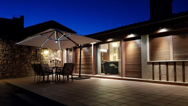 An outdoor patio area with a stone wall, a table with chairs, and a large umbrella providing shade.