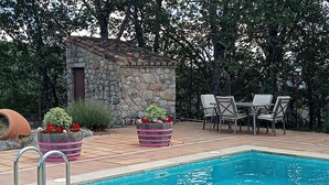 A swimming pool with stone walls, outdoor seating, and potted plants.