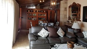 A cozy living room with a leather sofa, patterned cushions, a wooden bookshelf, and a decorative mirror.