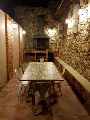 Eine Terrasse im Freien mit einer Steinsäule, einem Kamin aus Ziegeln und einem mit Stühlen umgebenen Tisch mit Fliesen.
