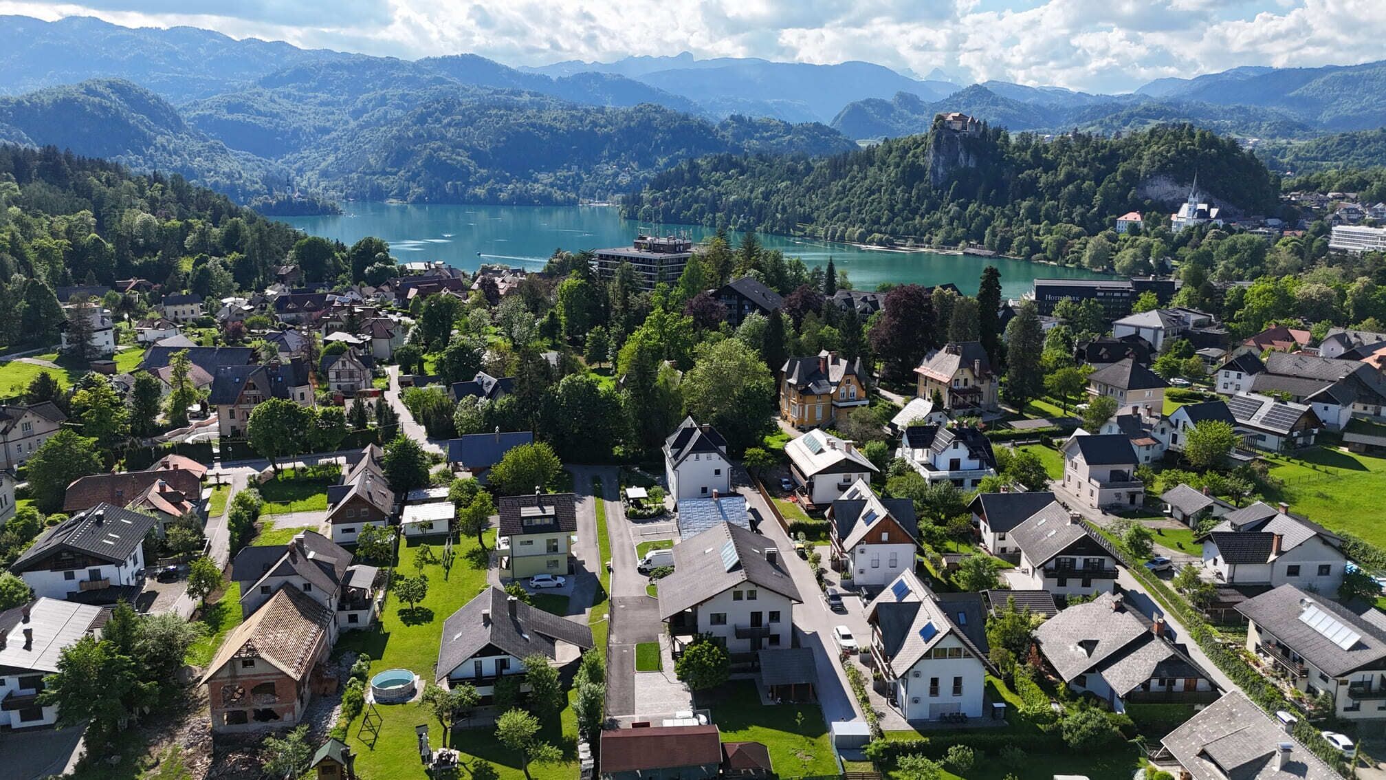 A residential area with houses, a swimming pool, and a lake in the background.