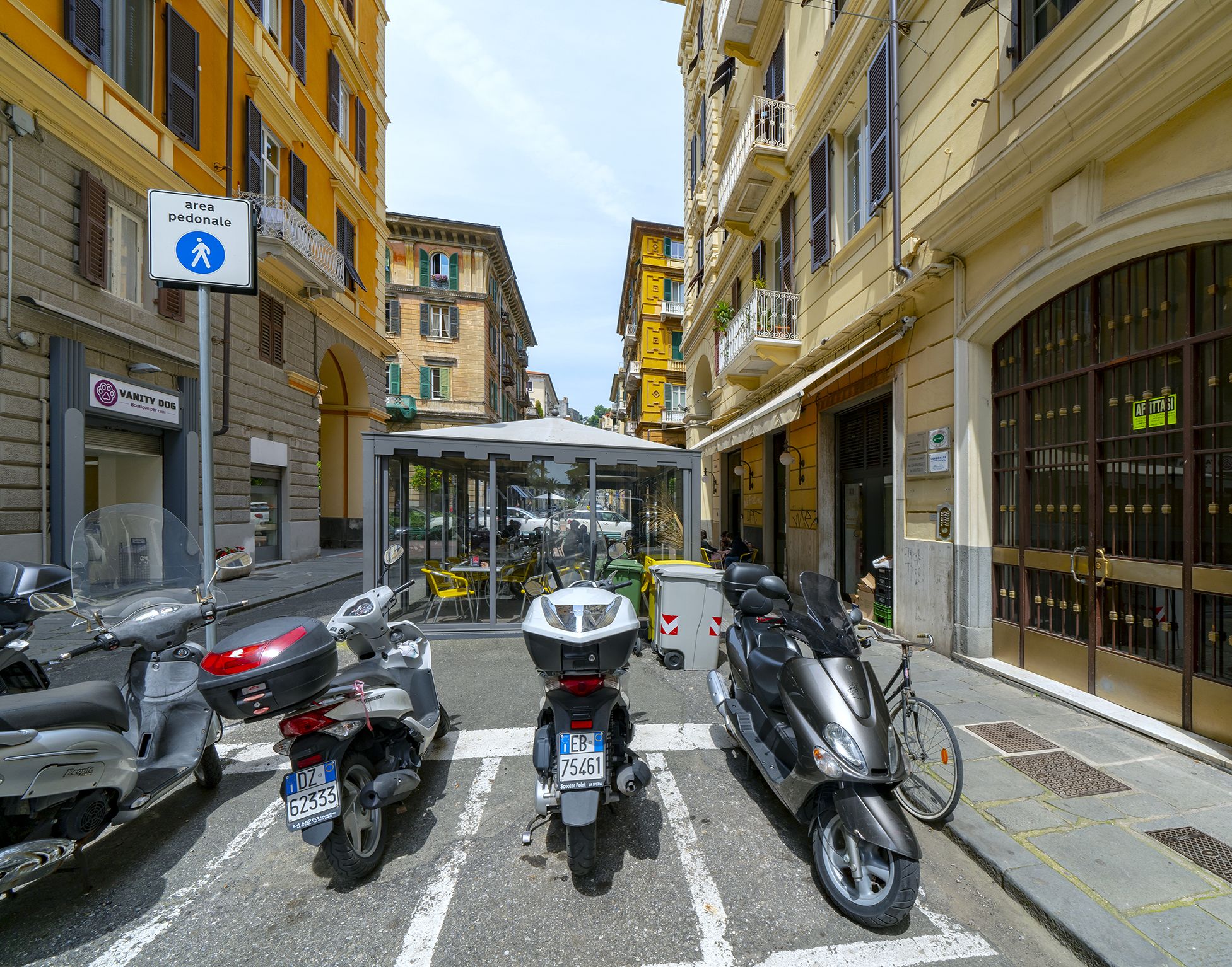 A street with parked scooters and a pedestrian crossing sign.