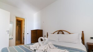 Une chambre à coucher comprenant un lit, une tête de lit en bois, une armoire et une porte donnant sur une salle de bain.
