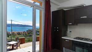 Une cuisine avec des meubles de couleur sombre, une cuisinière à gaz et une vue sur la mer, visible à travers une porte-fenêtre coulissante.