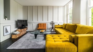 Ein modernes Wohnzimmer mit einem gelben Sofa, einem Glastisch, einer Holz-Unterhaltungsecke und einem großen Fenster.