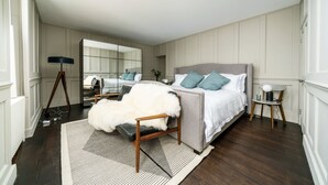 Ein Schlafzimmer mit einem großen Bett, einem Sessel mit einem Fellüberwurf, einem kleinen Tisch mit einer Lampe und einem Spiegel an der Wand.