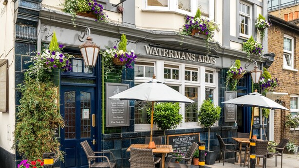 Eine Kneipe namens "Watermans Arms" mit Außenbestuhlung und hängenden Blumenkörben.