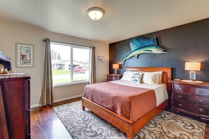 Un dormitorio con una cama grande, un aparador de madera, una mesita de noche, una lámpara de pared, una ventana con cortinas y un mural decorativo de peces.