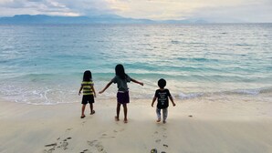 Three children walking on a sandy beach with footprints, facing the ocean.