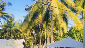 A gated entrance with a sign reading "Stay Relax With Tropical Vibes," surrounded by lush greenery and palm trees.
