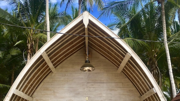 A bungalow with a triangular roof, a bed, and a balcony.