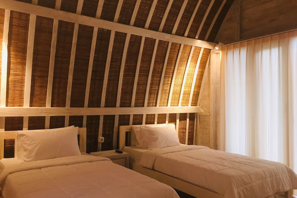 A room with two beds, wooden ceiling beams, and a window with curtains.