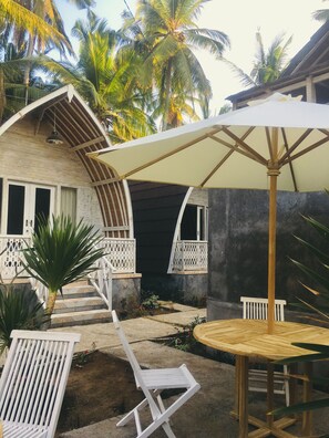 A covered outdoor seating area with a table and chairs, a wooden bench, and a staircase leading to a building with a number '3' sign. - The Vagary Vibes (Penida Island)