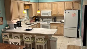 A kitchen with wooden cabinets, a white refrigerator, a microwave, a stove, and a sink. There are four white chairs around a wooden table. - Fantastic Oceanfront Home/Lgprivpool/Wifi/A+Location-Call/text 4046643546 (Gulf Shores)