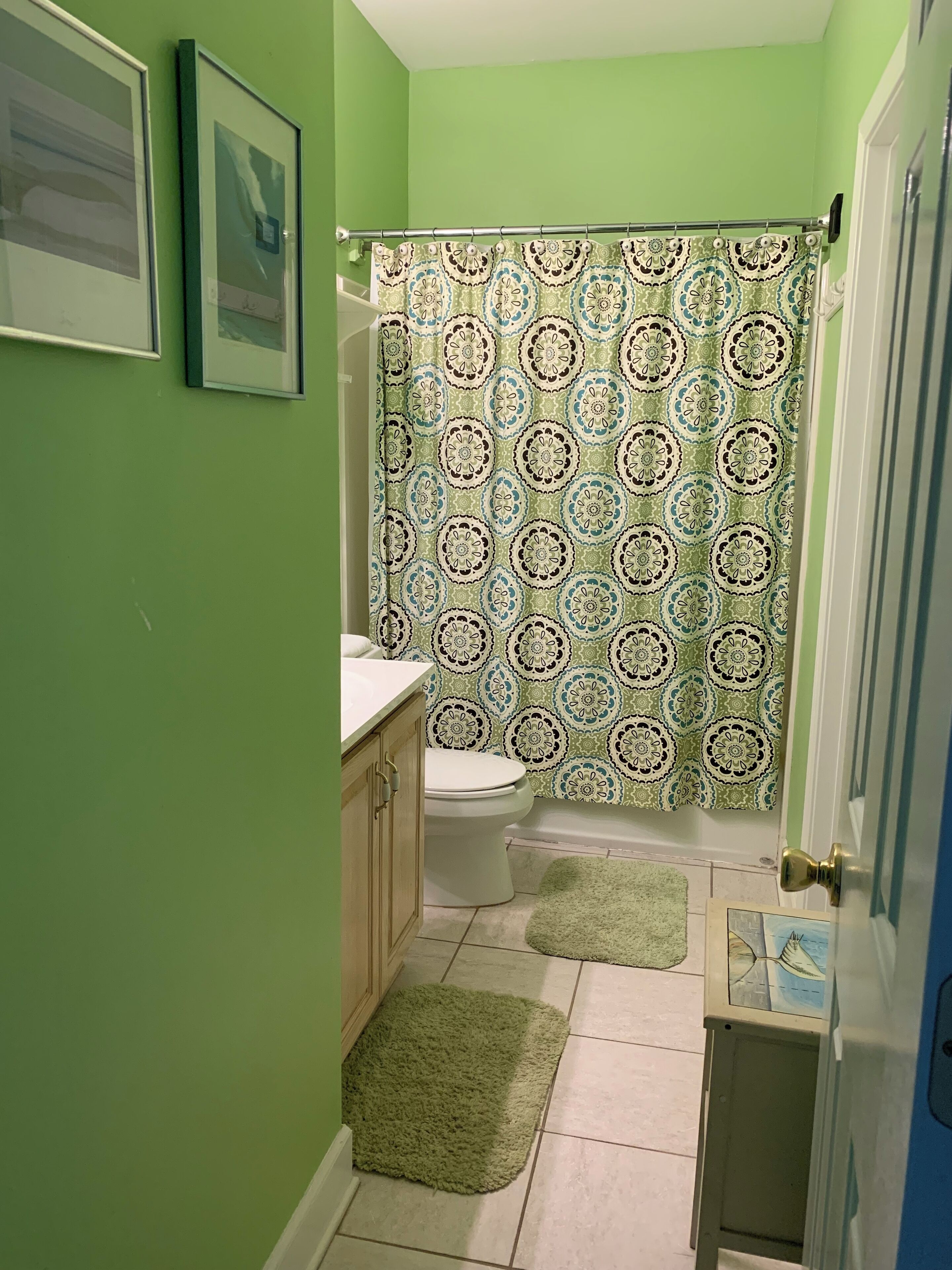 Een badkamer met groene wanden, een gordijn met een patroon voor de douche, een toilet en een klein vloerkleed.