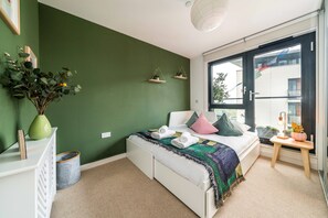 A bedroom with a bed, a nightstand, a window, and a view of the outside. - Neumann (London)