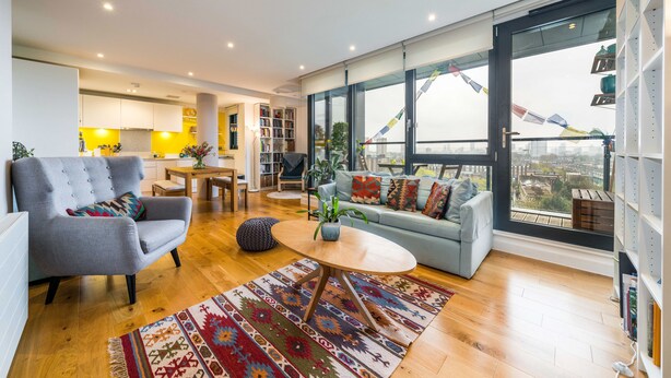 A spacious living area with a sofa, armchair, and coffee table, a dining area with a table and chairs, and large windows offering a city view. - Neumann (London)