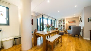 A spacious living area with a wooden dining table, a grey armchair, and a bookshelf. - Neumann (London)