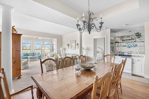 A spacious dining area with a wooden table and chairs, a chandelier, and a view of the living room and kitchen.