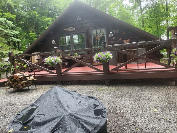 En stuga med en träveranda, en möblerad uteplats under tak och hängande blomkorgar.