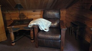 A wooden-paneled room with a leather armchair, a small wooden table, and a lamp. - Quiet country setting awaits you! (Munnsville)