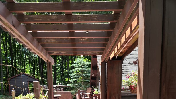 A wooden deck leading to a covered patio area with outdoor furniture and a garden. - Quiet country setting awaits you! (Munnsville)