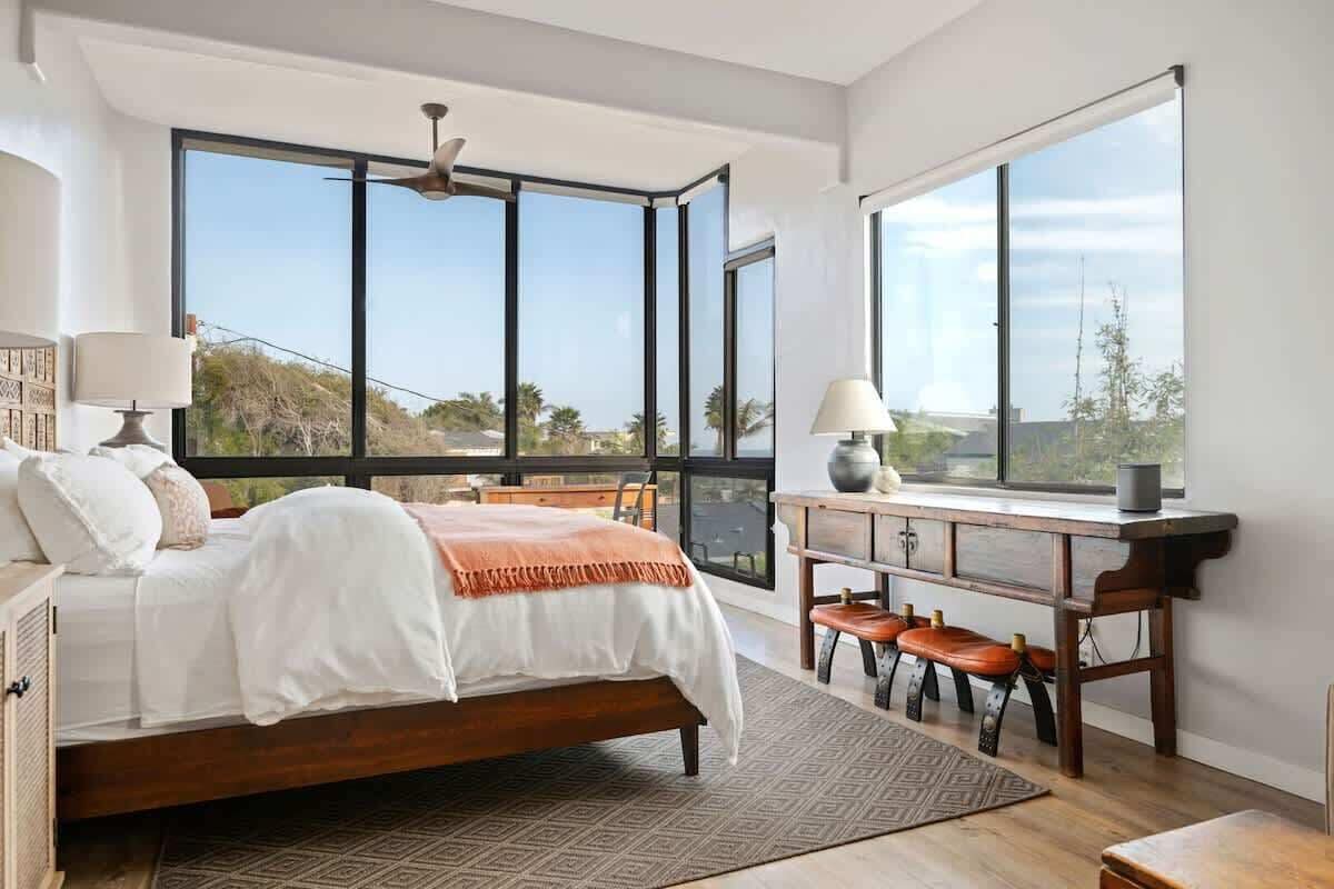 Quarto com cama grande, escrivaninha com cadeira e vista através de amplas janelas.