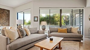 A modern living room with two sofas, a coffee table, and a large window with a view of greenery. - Padaro Beach Contemporary (Carpinteria)