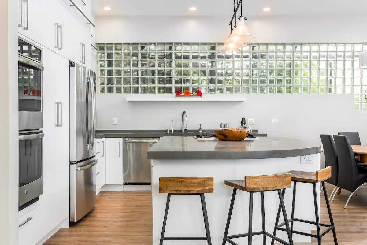 A modern kitchen with a central island, stainless steel appliances, and a green-tiled backsplash.