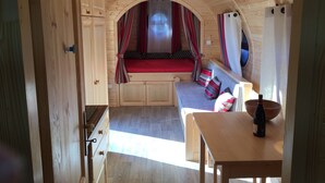Interior acolhedor de uma cabana de madeira, com uma cama, uma mesa e uma garrafa de vinho.