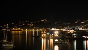 A nighttime coastal town with calm waters reflecting lights, a marina with boats, and buildings with illuminated windows. - Iconic Windmill in Mykonos (Mykonos)
