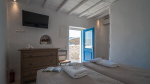 A bedroom with a wooden dresser, a bed with two pillows, a book, and a blue door leading outside. - Iconic Windmill in Mykonos (Mykonos)