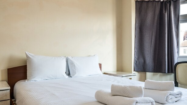 A neatly made bed with white linens, a pillow, and two rolled towels on the bed.