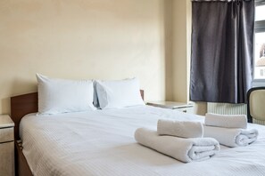 A neatly made bed with white linens, a pillow, and two rolled towels on the bed. - Kadiwar (London)