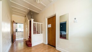 A hallway with wooden flooring, a white staircase, and a closed door with a sign.