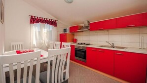 A compact kitchen with red cabinets, white countertops, a gas stove, and a sink. - House Boze (Vinisce)