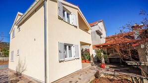 A two-story building with a beige exterior, multiple windows with shutters, and a tiled patio area with potted plants. - House Boze (Vinisce)