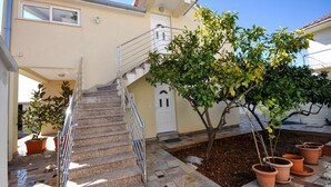A building with a staircase leading to a white door, surrounded by potted plants and a tiled patio area. - House Boze (Vinisce)
