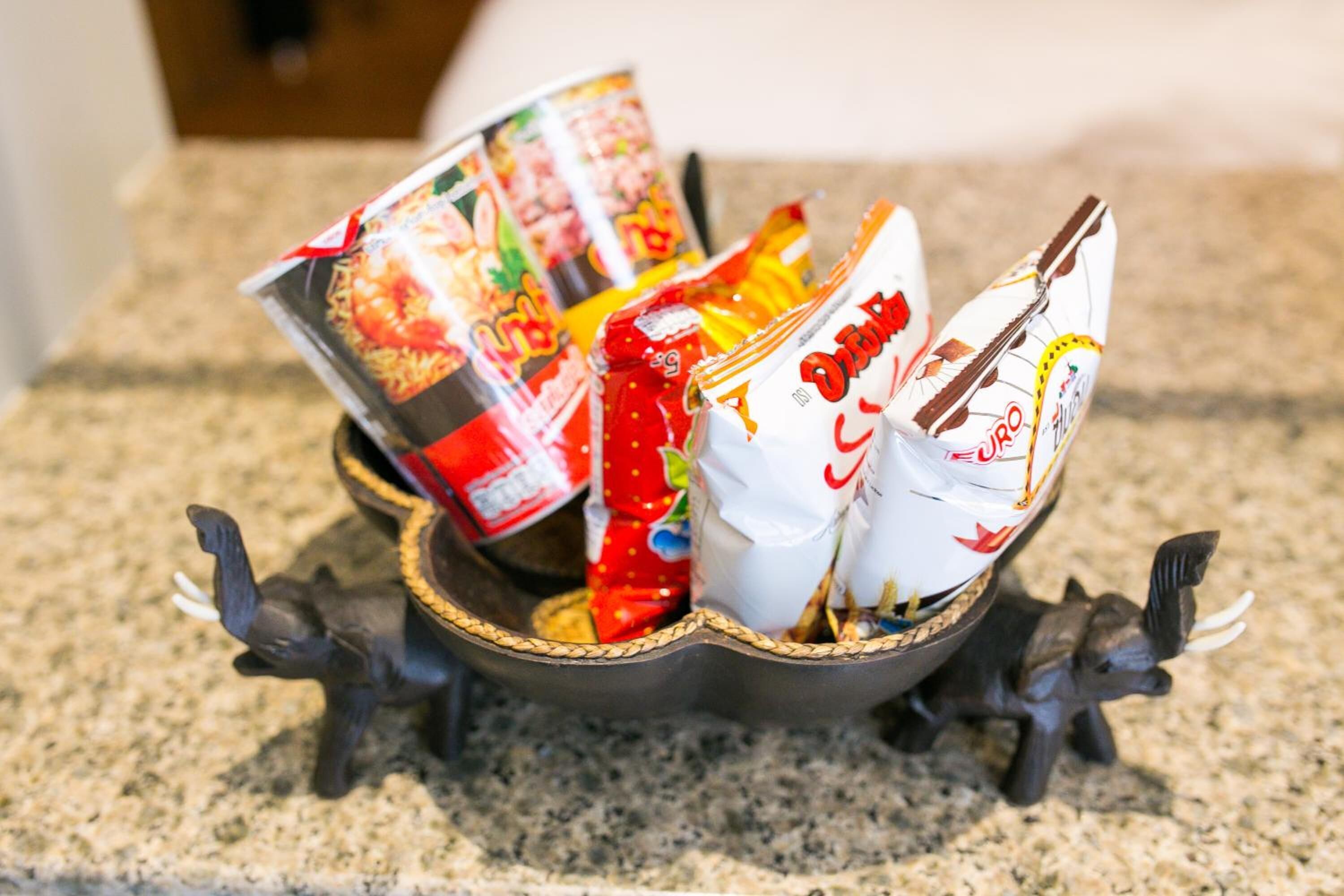 A decorative bowl with various packaged snacks on a granite countertop.