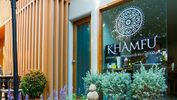 Een restaurantingang met een stenen pad dat naar de deur leidt, potplanten en een moderne gevel.